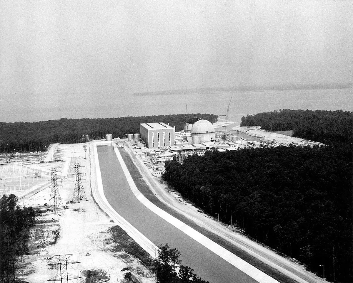 Aerial black-and-white view of the Surry Power Station in Virginia under construction beside a canal and transmission towers